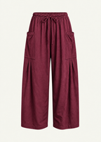 Front product view of the Rouge Bailey Pant by Lunetti against an ivory background, featuring rich burgundy bamboo cotton fabric, a relaxed wide-leg silhouette, elastic drawstring waistband, and symmetrical oversized cargo pockets with pleated detailing.