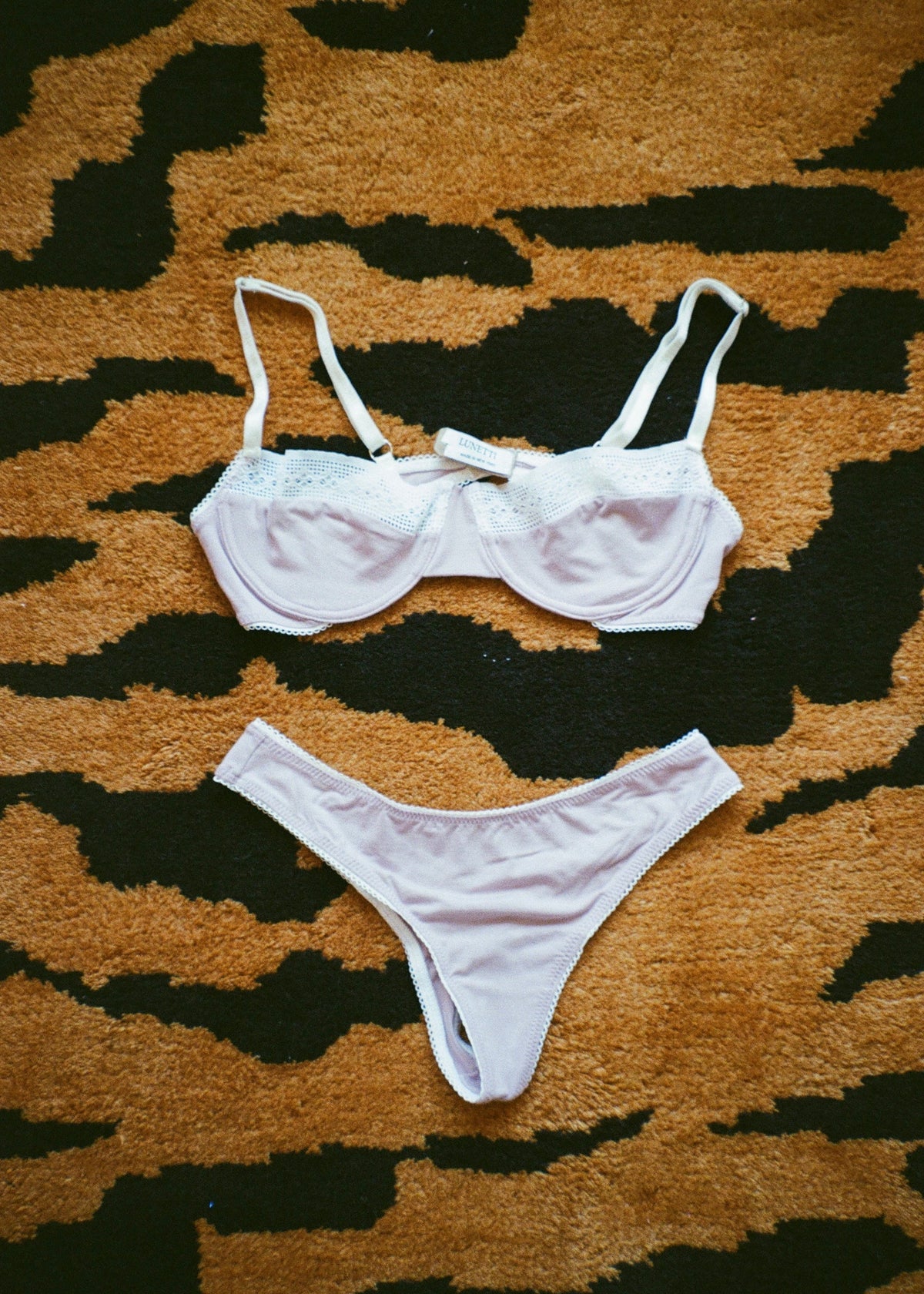 Lilac Charlotte Set by Lunetti paired with the matching underwire bra, arranged on a mustard yellow and black patterned rug, showcasing the soft bamboo jersey fabric and delicate white lace trim.