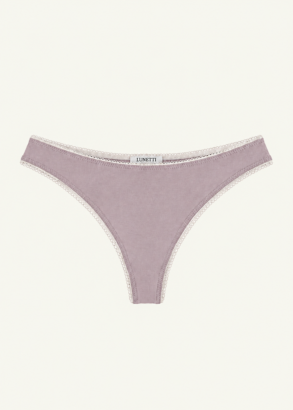 Front product view of the Lilac Charlotte Thong by Lunetti against an ivory background, featuring soft lilac bamboo jersey, delicate ivory picot lace trim along the waistband and leg openings, and a centered Lunetti label.