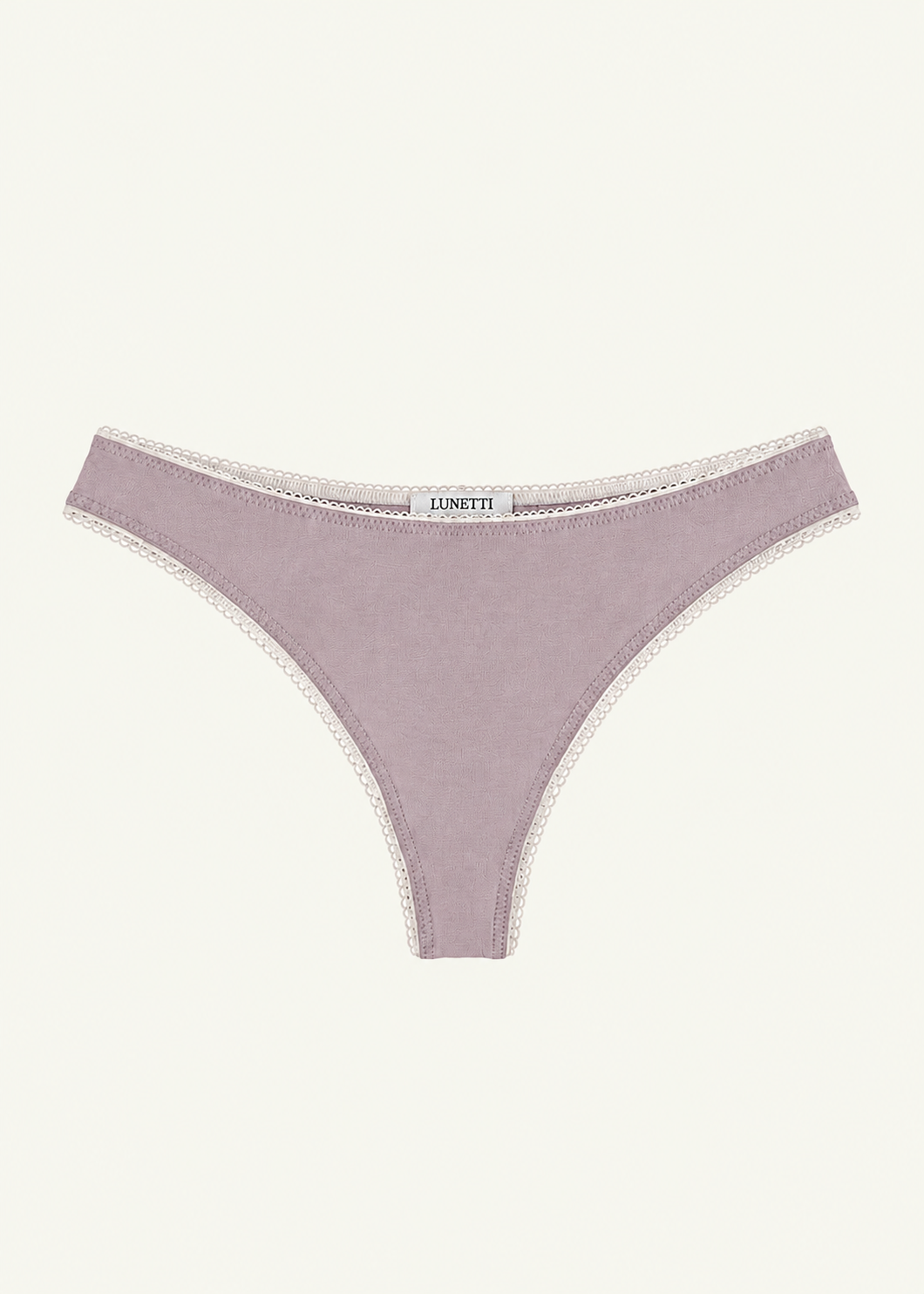 Front product view of the Lilac Charlotte Thong by Lunetti against an ivory background, featuring soft lilac bamboo jersey, delicate ivory picot lace trim along the waistband and leg openings, and a centered Lunetti label.