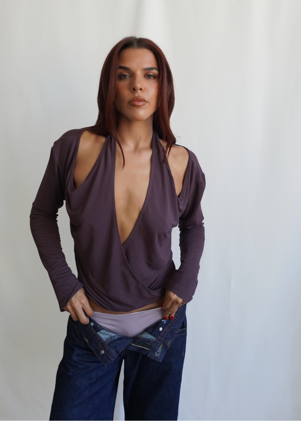 Front view of a model wearing the Amethyst Dahlia Top by Lunetti with blue jeans, showcasing the dramatic plunging crisscross neckline, softly draped bamboo jersey, and fitted long sleeves.