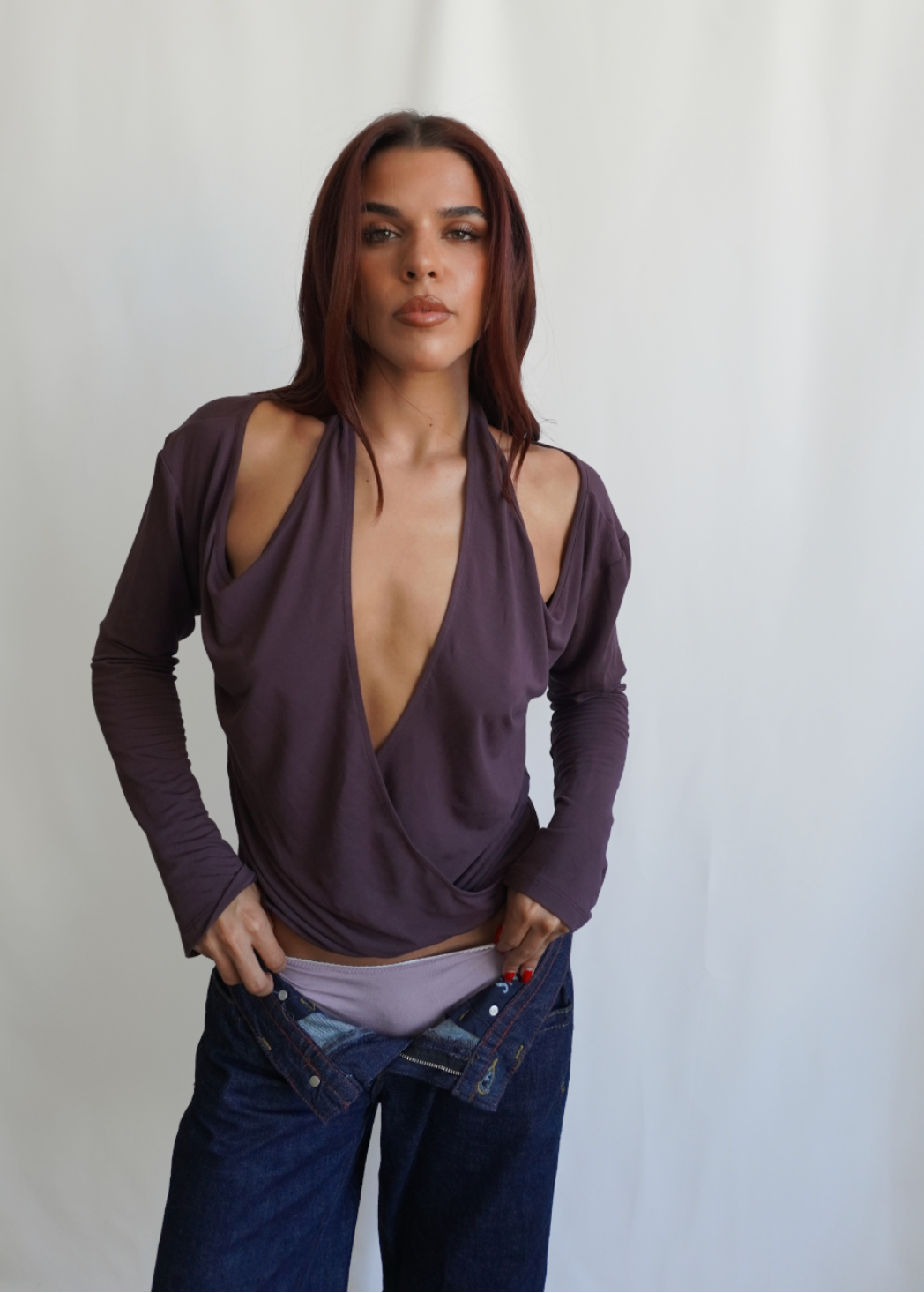 Front view of a model wearing the Amethyst Dahlia Top by Lunetti with blue jeans, showcasing the dramatic plunging crisscross neckline, softly draped bamboo jersey, and fitted long sleeves.