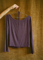 Amethyst Dahlia Top by Lunetti hanging on a wire hanger against a warm brown curtain, showcasing its long sleeves, soft bamboo jersey fabric, and relaxed neckline.