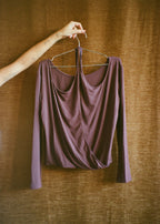 Orchid Dahlia Top by Lunetti hanging against a brown curtain backdrop, showcasing the softly draped neckline, fluid shape, and long sleeves.