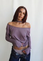 Model wearing the Orchid Dahlia Top by Lunetti with blue jeans, styled off the shoulders to highlight the versatile draped neckline and soft bamboo jersey fabric.