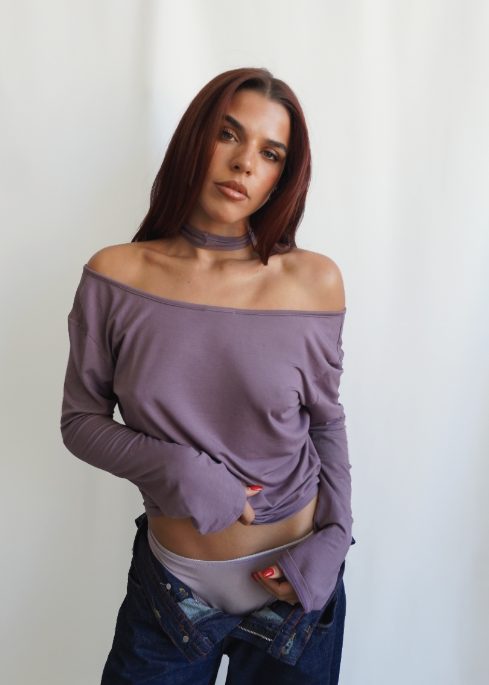 Model wearing the Orchid Dahlia Top by Lunetti with blue jeans, styled off the shoulders to highlight the versatile draped neckline and soft bamboo jersey fabric.