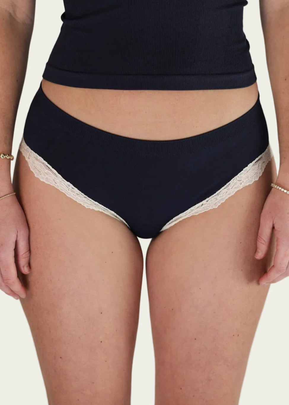 Front view of a model wearing the Midnight Navy Luna Brief by Lunetti with a matching camisole, showcasing the mid-rise waistband and ivory lace-trimmed leg openings.