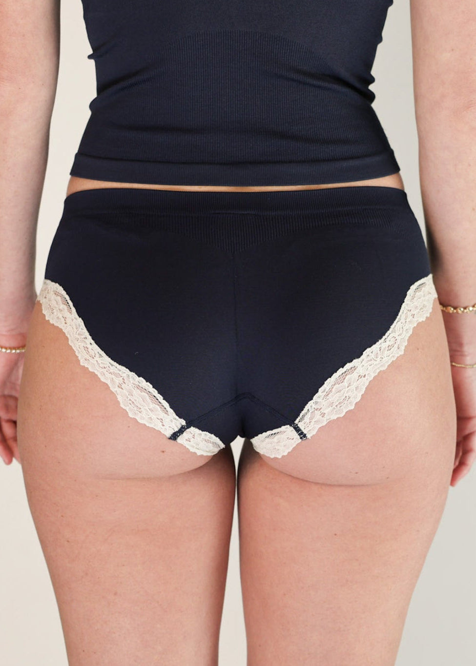 Rear view of a model wearing the Midnight Navy Luna Brief by Lunetti, highlighting the full back coverage and delicate ivory lace edging.