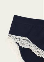 Close-up of the Midnight Navy Luna Brief by Lunetti against an ivory background, showcasing the smooth navy fabric, waistband stitching, and scalloped ivory floral lace trim.