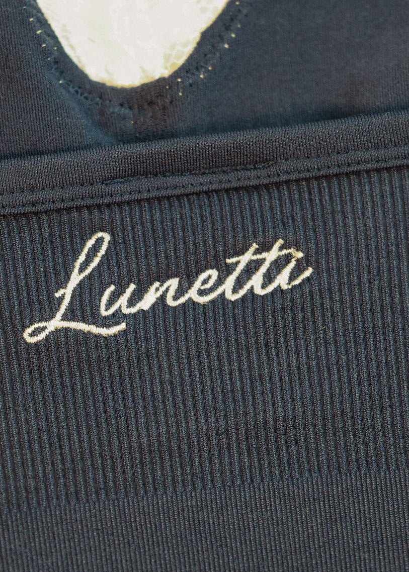 Close-up of the Luna Cami by Lunetti in Midnight Navy, showcasing the signature ivory Lunetti embroidery on textured navy fabric beneath the lace-trimmed neckline.