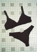 Black bamboo jersey Margot Bralette and matching thong by Lunetti arranged on a pale green tiled floor, showcasing the coordinating wireless lingerie set.