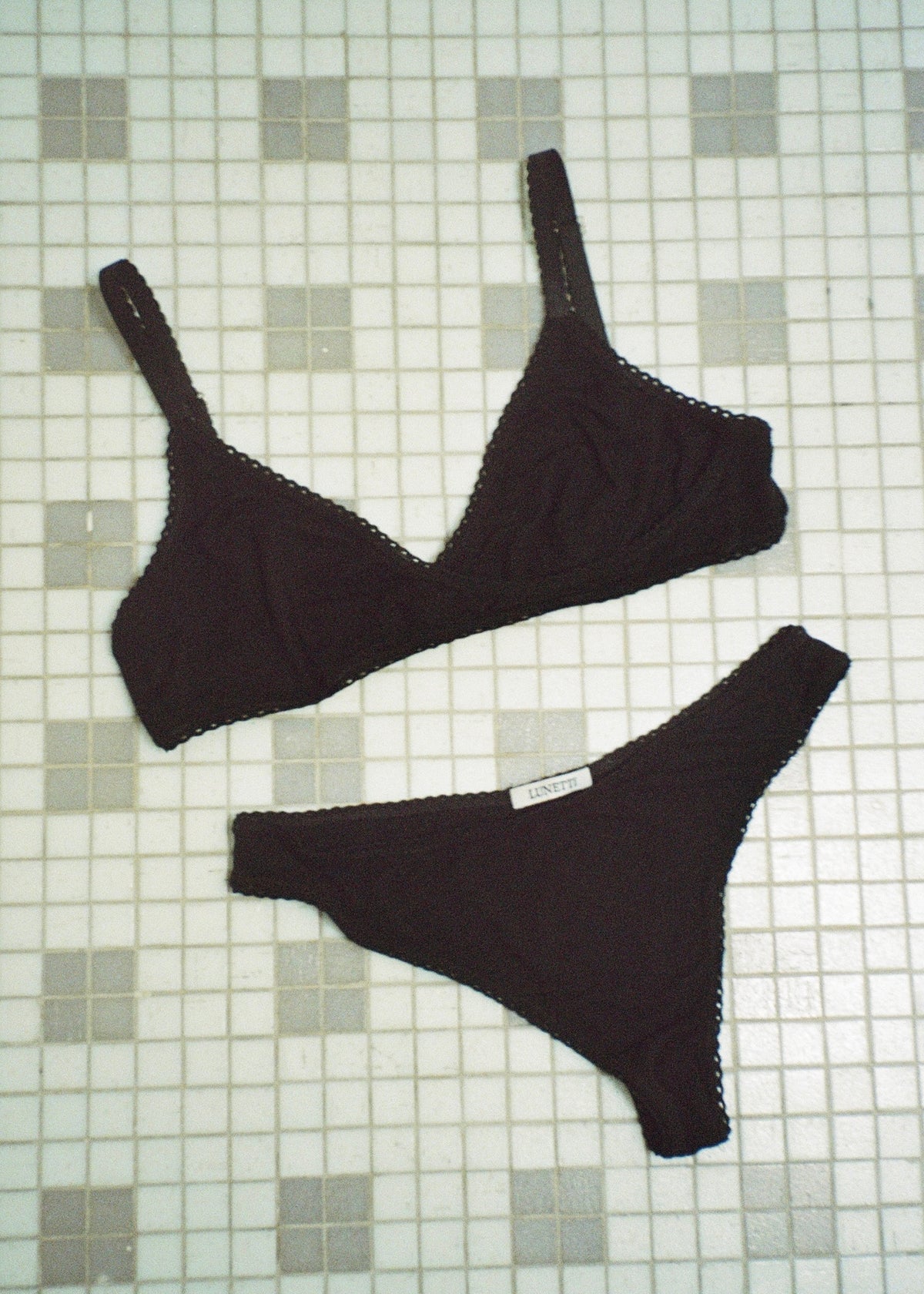 Black bamboo jersey Margot Bralette and matching thong by Lunetti arranged on a pale green tiled floor, showcasing the coordinating wireless lingerie set.
