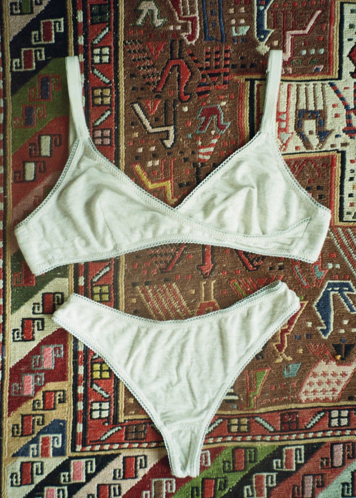 Heather grey Margot Thong by Lunetti paired with a matching bralette, arranged on a colorful patterned vintage rug, showcasing the coordinating bamboo jersey underwear set.