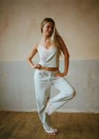 Model posing with one leg raised wearing the Coastal Blue Paloma Pant by Lunetti and a white camisole, highlighting the soft Pima cotton fabric, drawstring waistband, and wide-leg silhouette.
