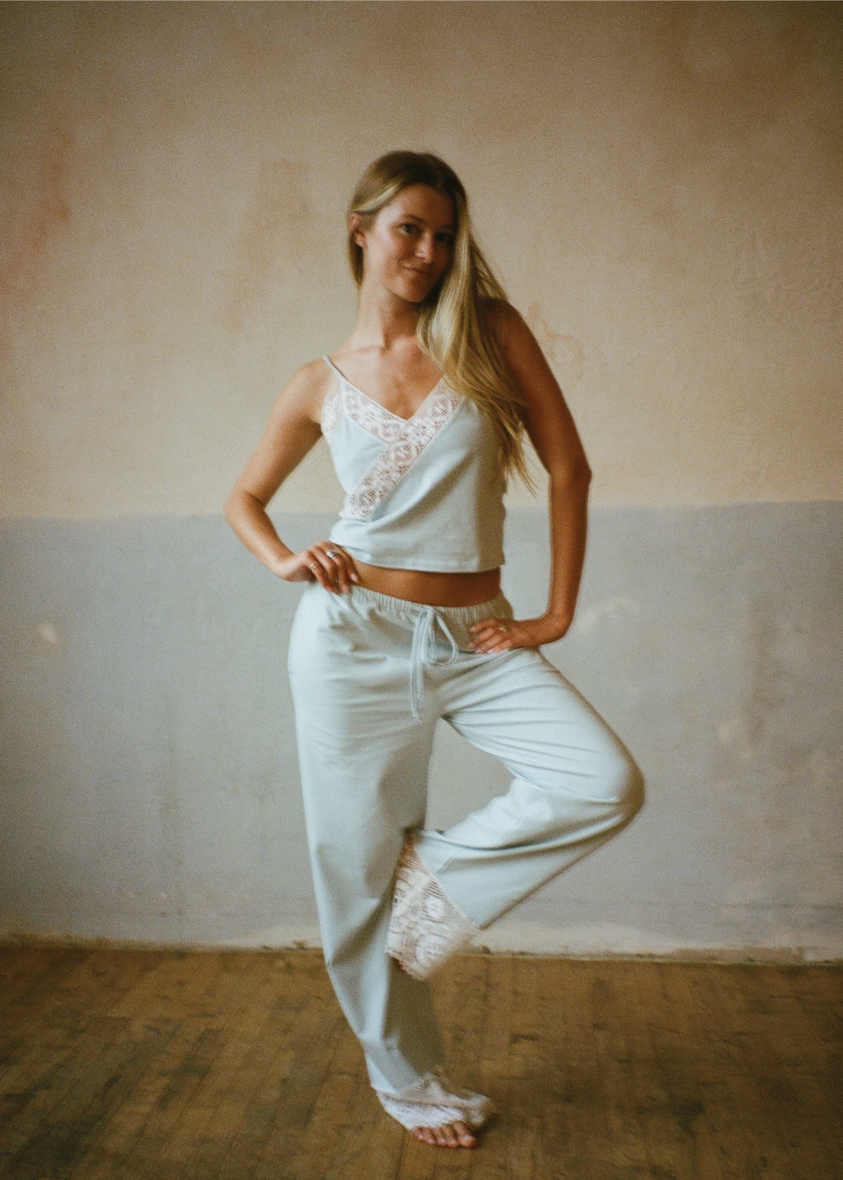 Model posing with one leg raised wearing the Coastal Blue Paloma Pant by Lunetti and a white camisole, highlighting the soft Pima cotton fabric, drawstring waistband, and wide-leg silhouette.