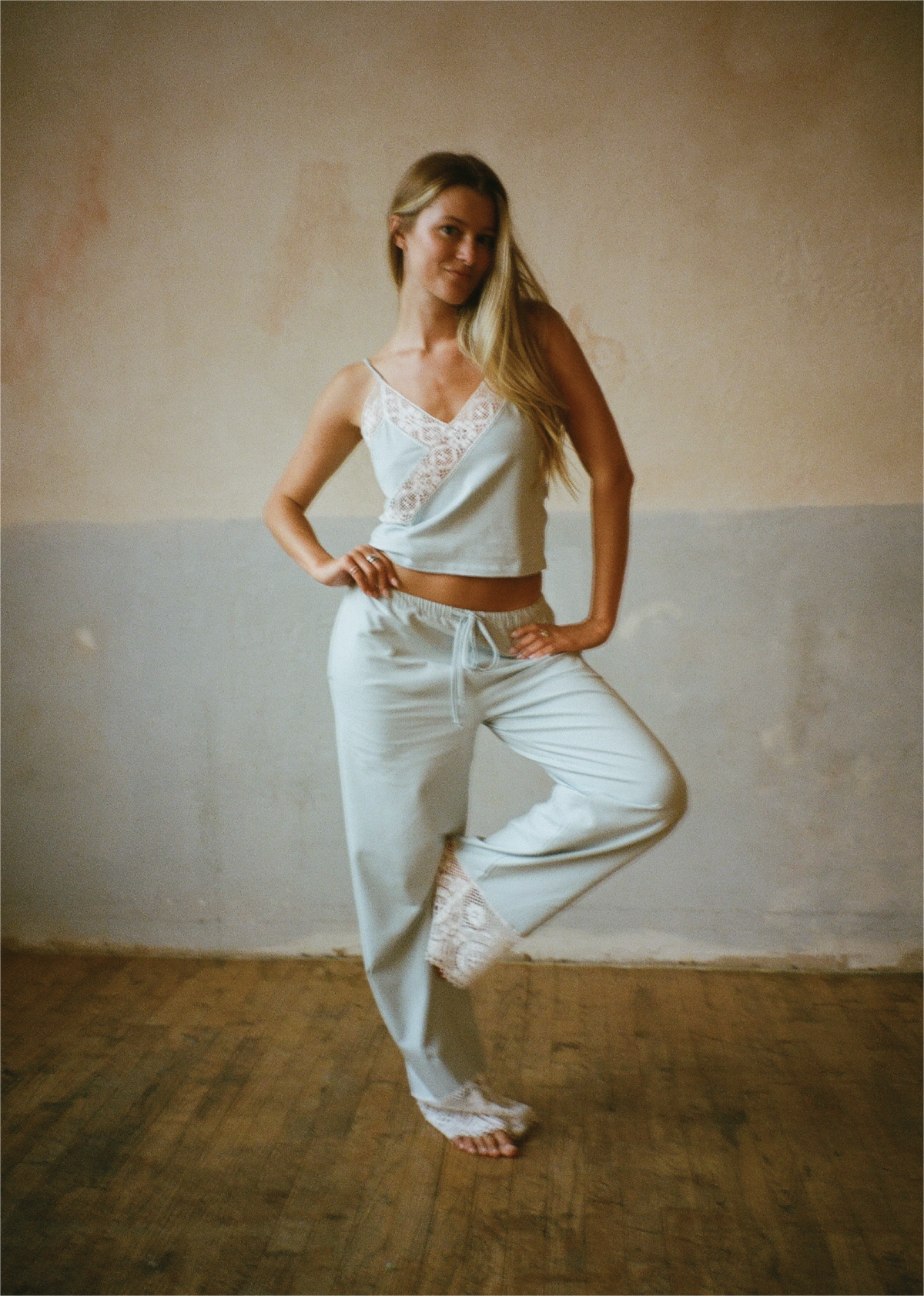 Model posing with one leg raised wearing the Coastal Blue Paloma Top and matching wide-leg pants by Lunetti, standing barefoot against a textured studio wall.
