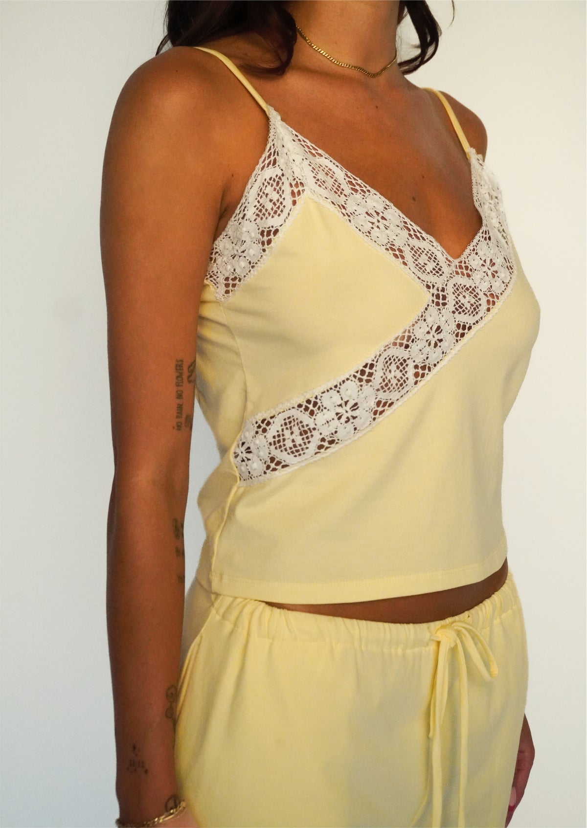 Close-up of a model wearing the Honeycomb Paloma Top by Lunetti, highlighting the intricate white cotton lace panels across the V-neckline and diagonally along the front.