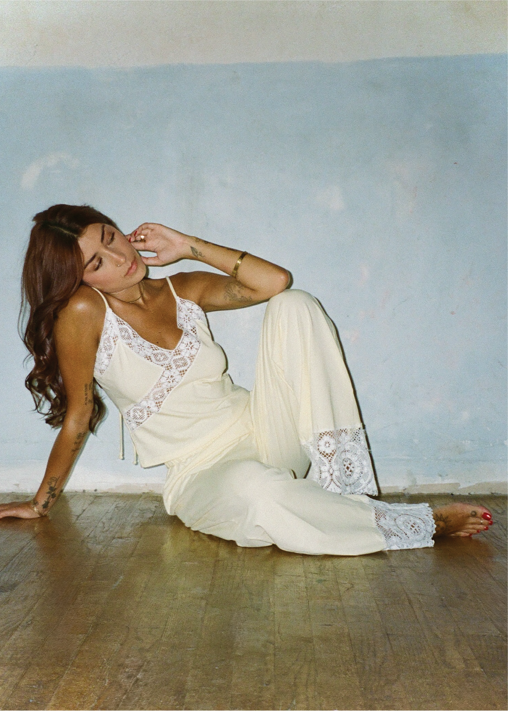 Model sitting barefoot on a wooden floor wearing the Honeycomb Paloma Top with matching wide-leg pants, leaning against a pale blue wall in a relaxed pose.