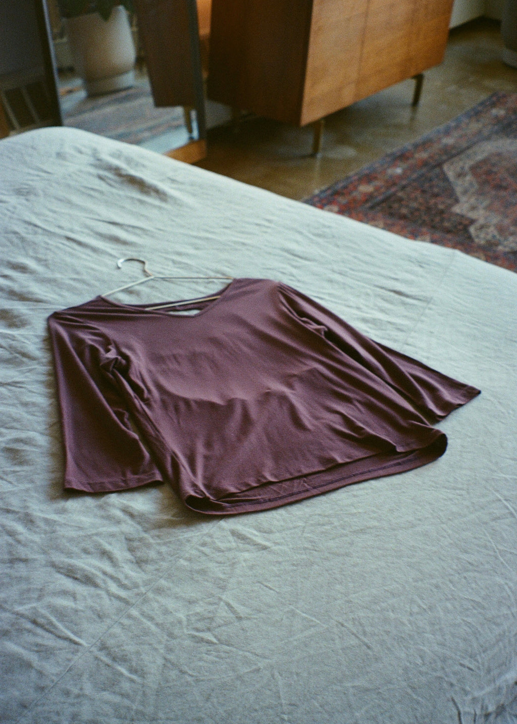 Amethyst bamboo jersey Willow Top by Lunetti laid flat on a soft blue bedspread, showcasing its V-neckline, three-quarter sleeves, and relaxed silhouette.