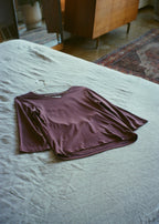 Amethyst bamboo jersey Willow Top by Lunetti laid flat on a soft blue bedspread, showcasing its V-neckline, three-quarter sleeves, and relaxed silhouette.