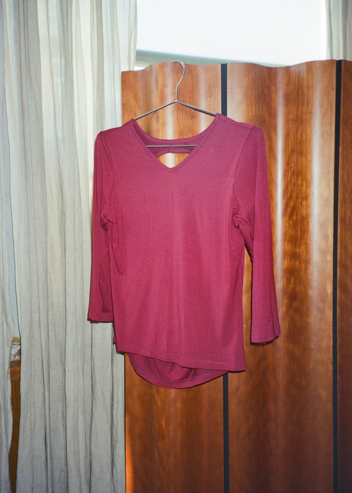 Merlot bamboo jersey Willow Top by Lunetti hanging on a wire hanger against a wooden folding screen, featuring a V-neckline and three-quarter sleeves.