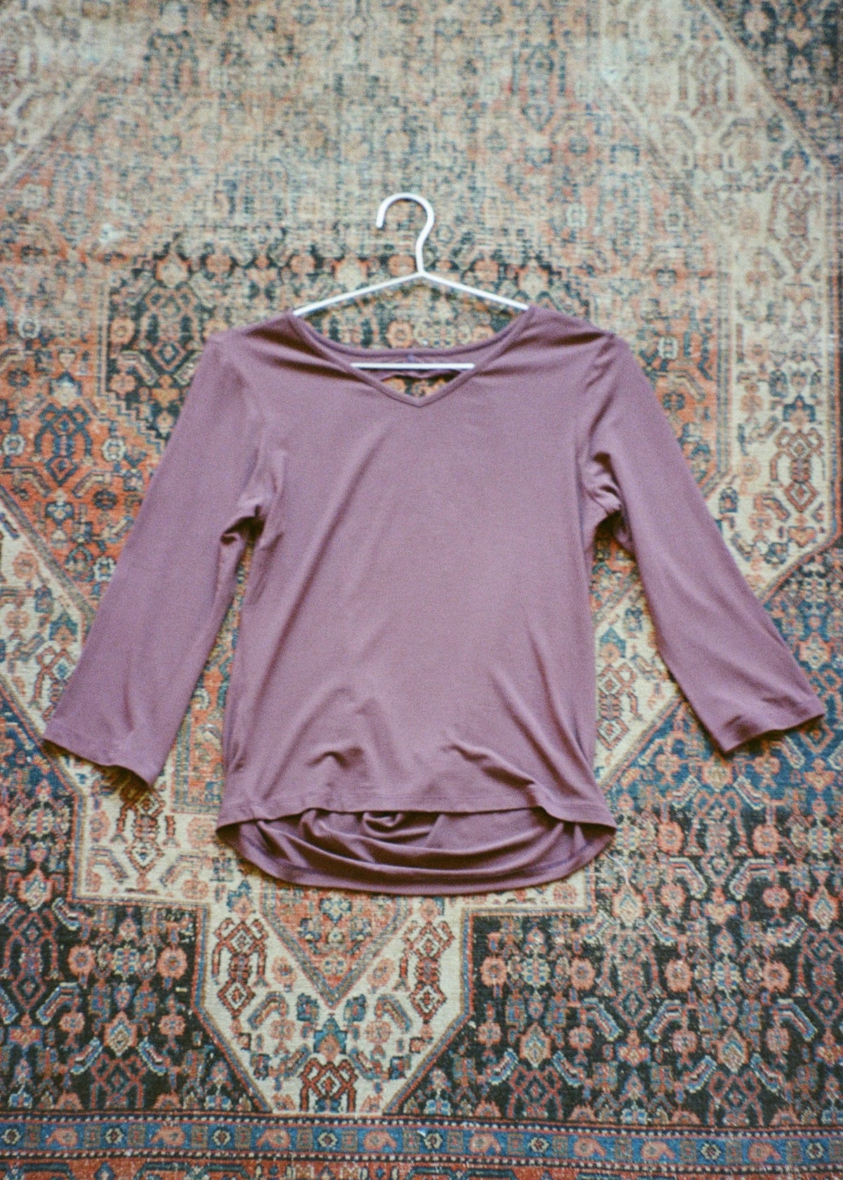 Orchid bamboo jersey Willow Top by Lunetti displayed on a hanger against a patterned vintage rug, showcasing its V-neckline, three-quarter sleeves, and relaxed silhouette.
