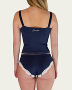 Back view of model wearing the Lunetti Luna Top and Luna Brief in Midnight Navy with white lace trim and logo embroidery across the back of the top.